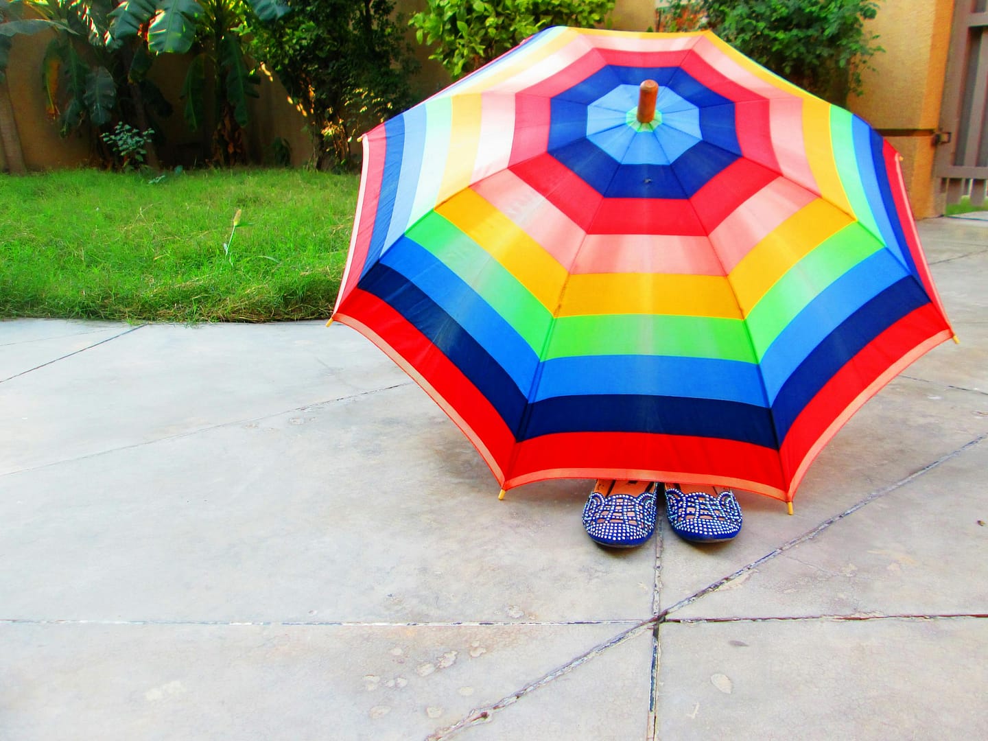 Bright and colorful rainbow umbrella shading patterned shoes on a sunny day.